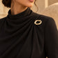 Model wearing a black high-neck draped gown styled with Tie Shop Chunky Gold Organic Ring Brooch on the shoulder, a modern chic fashion brooch. موديل ترتدي فستان أسود أنيق بياقة مرتفعة مزين بـ بروش سميك ذهبي بتصميم حلقة مموجة من تاي شوب، لمسة راقية للملابس.اكتشفي أناقة بروش تاى شوب مع الحجاب والملابس