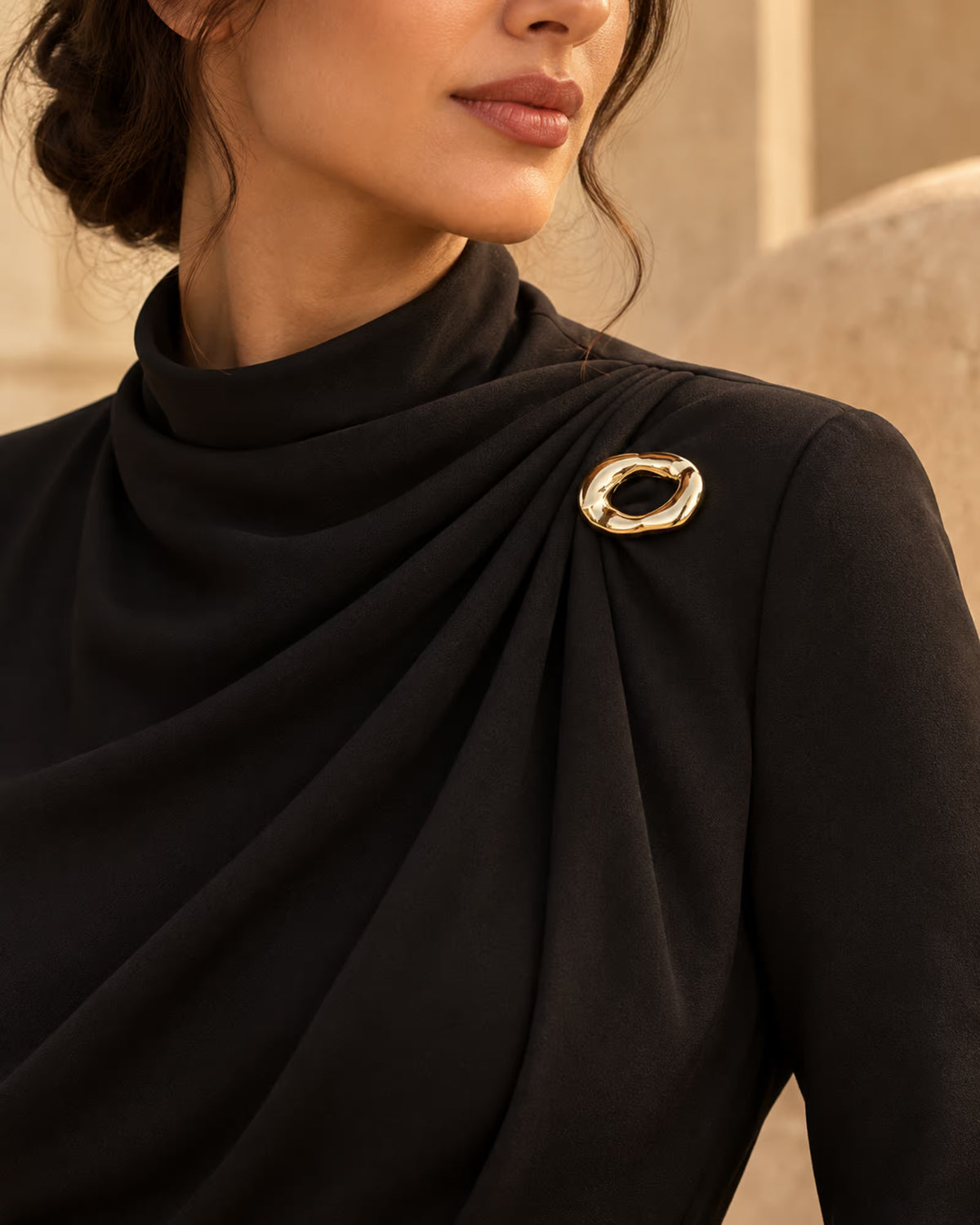 Model wearing a black high-neck draped gown styled with Tie Shop Chunky Gold Organic Ring Brooch on the shoulder, a modern chic fashion brooch. موديل ترتدي فستان أسود أنيق بياقة مرتفعة مزين بـ بروش سميك ذهبي بتصميم حلقة مموجة من تاي شوب، لمسة راقية للملابس.اكتشفي أناقة بروش تاى شوب مع الحجاب والملابس