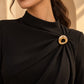 Model wearing a black formal draped dress styled with Tie Shop Gold Wavy Textured Ring Brooch, a luxury brooch accessory for women's hijab and outfits. موديل ترتدي فستان أسود أنيق مزين بـ بروش نسائي من تاي شوب بتصميم حلقة ذهبية مموجة ومطروقة، إكسسوار أنيق للحجاب والملابس.