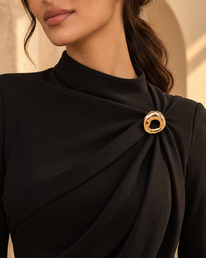Model wearing a black formal draped dress styled with Tie Shop Gold Wavy Textured Ring Brooch, a luxury brooch accessory for women's hijab and outfits. موديل ترتدي فستان أسود أنيق مزين بـ بروش نسائي من تاي شوب بتصميم حلقة ذهبية مموجة ومطروقة، إكسسوار أنيق للحجاب والملابس.