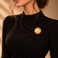 Model wearing an elegant black draped dress styled with Tie Shop Smooth Gold Disc Brooch on the chest, a luxury minimalist brooch accessory for women's hijab and outfits. موديل ترتدي فستان أسود أنيق مزين بـ بروش نسائي من تاي شوب بتصميم دائري ذهبي مصقول، إكسسوار أنيق للحجاب والملابس.