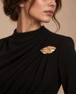 Model wearing a black formal draped dress styled with Tie Shop Abstract Gold Wave Leaf Brooch, a luxury brooch accessory for women's hijab and outfits. موديل ترتدي فستان أسود أنيق مزين بـ بروش نسائي من تاي شوب بتصميم ورق شجر ذهبي مموج، إكسسوار أنيق للحجاب والملابس.
