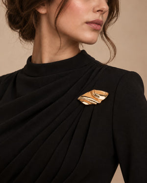 Model wearing a black formal draped dress styled with Tie Shop Abstract Gold Wave Leaf Brooch, a luxury brooch accessory for women's hijab and outfits. موديل ترتدي فستان أسود أنيق مزين بـ بروش نسائي من تاي شوب بتصميم ورق شجر ذهبي مموج، إكسسوار أنيق للحجاب والملابس.