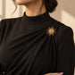 Tie Shop Gold Sunburst Brooch on black high-neck dress. بروش نسائي من تاي شوب بتصميم شمس ذهبية على فستان أسود أنيق، إكسسوار أنيق للحجاب والملابس.