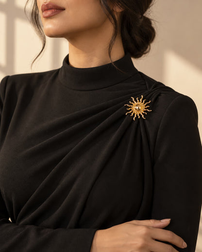 Tie Shop Gold Sunburst Brooch on black high-neck dress. بروش نسائي من تاي شوب بتصميم شمس ذهبية على فستان أسود أنيق، إكسسوار أنيق للحجاب والملابس.