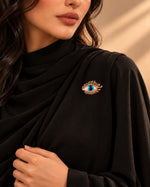Model wearing a black formal dress accessorized with Tie Shop Gold Blue Eye Crystal Brooch, a stylish pin for abayas and dresses. موديل ترتدي فستان أسود أنيق مزين بـ بروش العين الزرقاء الذهبي من تاي شوب، دبوس عصري للعبايات والفساتين.