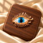 Close-up of Tie Shop Gold Blue Eye Crystal Brooch with detailed metallic eyelashes on a wooden base, a unique brooch for women. صورة مقربة لـ بروش العين الزرقاء الذهبي من تاي شوب مع رموش معدنية على قاعدة خشبية، بروش نسائي مميز.