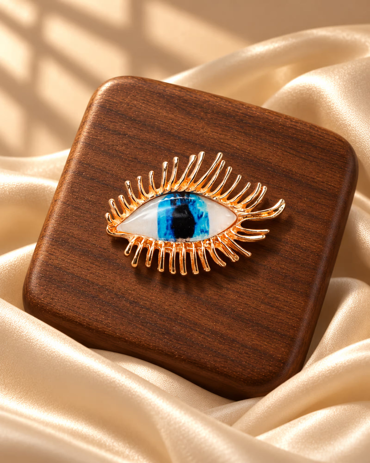 Close-up of Tie Shop Gold Blue Eye Crystal Brooch with detailed metallic eyelashes on a wooden base, a unique brooch for women. صورة مقربة لـ بروش العين الزرقاء الذهبي من تاي شوب مع رموش معدنية على قاعدة خشبية، بروش نسائي مميز.
